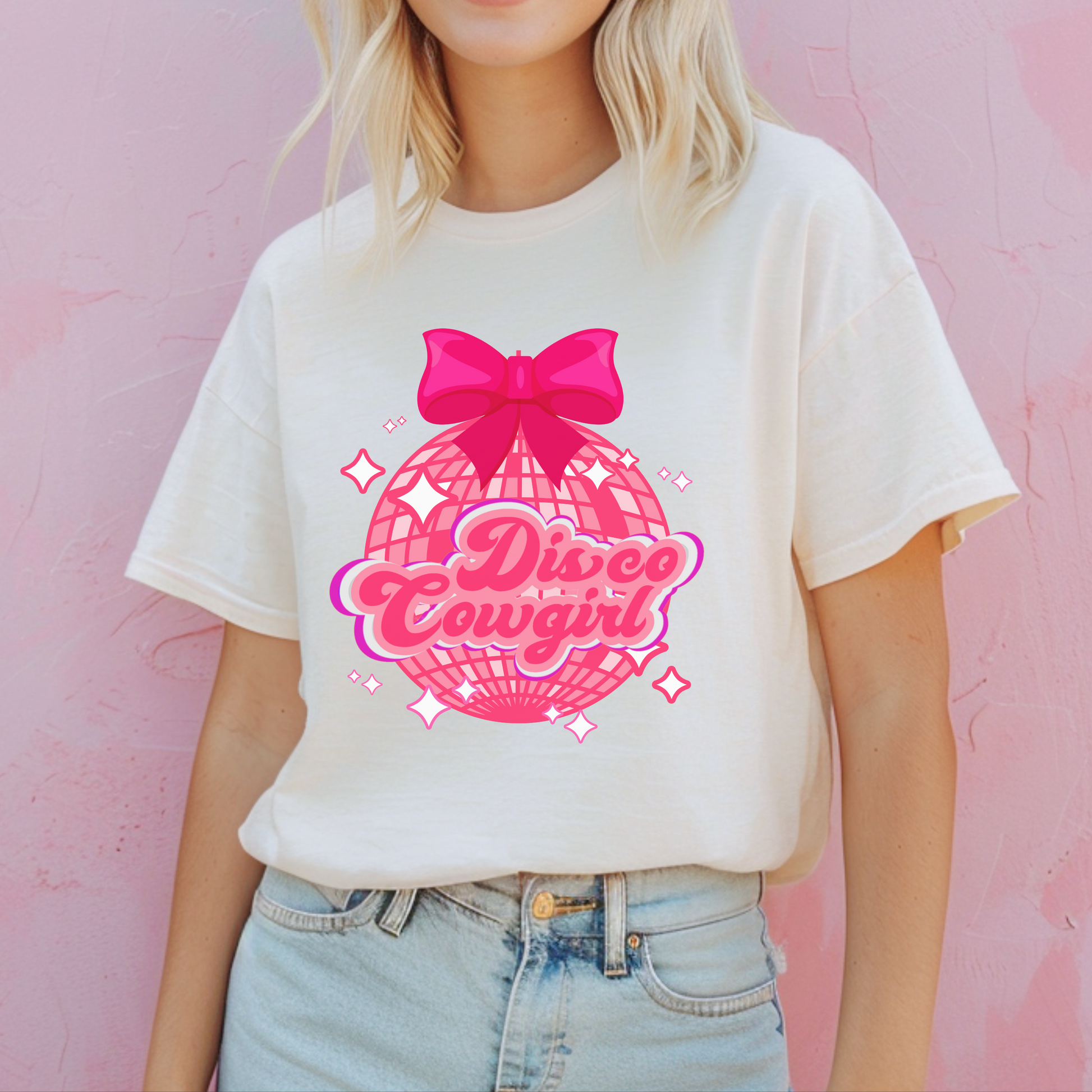 Women's Comfort Colors tee featuring a pink disco ball and script "Disco Cowgirl" text with a hot pink bow and scattered stars. This soft girl western-inspired shirt is a must-have for Nashville getaways, rodeo weekends, and girls' night celebrations. Designed for comfort and style in sizes S–4XL. A coquette, retro twist on classic western apparel.