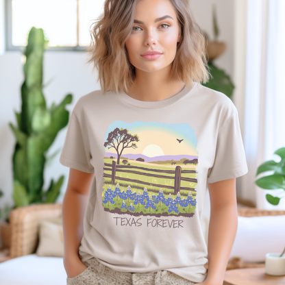 Image: A soft and stylish T-shirt showcasing a stunning Texas landscape with bluebonnets stretching across rolling hills under a fiery sunset sky. The phrase "Texas Forever" is printed across the design, making it an ideal statement piece for anyone who loves Texas. Whether heading to a rodeo, a state fair, or a country concert, this tee embodies Texas pride. A thoughtful and unique gift for native Texans or those who just love the Lone Star State, by jaecrece.