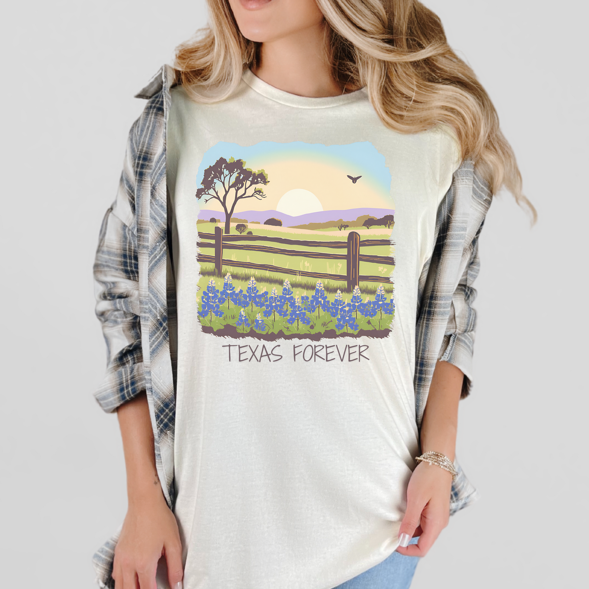 Image: Celebrate Texas heritage with this charming T-shirt featuring an artistic rendition of the Texas Hill Country. The graphic showcases a sprawling field of bluebonnets beneath a breathtaking sunset with "Texas Forever" inscribed in bold lettering. A great fit for Texas natives, lovers of country life, or those who appreciate wildflower season. Soft and comfortable, this tee pairs perfectly with denim or boots for a true western look, by jaecrece.