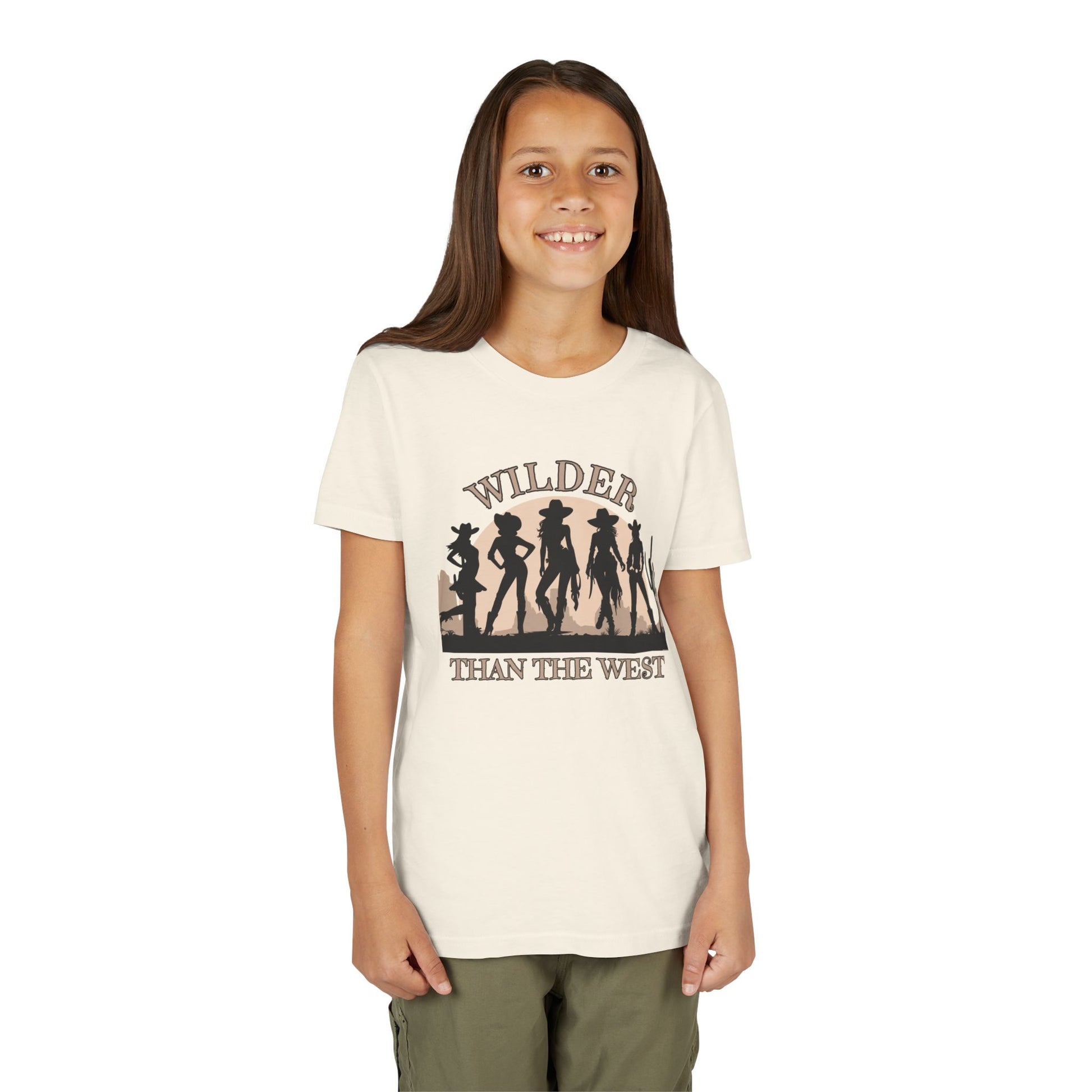 Youth girls western shirt in natural color featuring a strong “Wilder than the West” graphic with cowgirl silhouettes and a desert cactus sunset. Comes in sizes S–XL and is part of a fun mommy and me set for mini rodeo queens and southern girls. This vintage vibe tee is perfect for music festivals, horse lovers, Texas fairs, and bachelorette trip looks. Stylish graphic wear for bold, country-loving girls.
