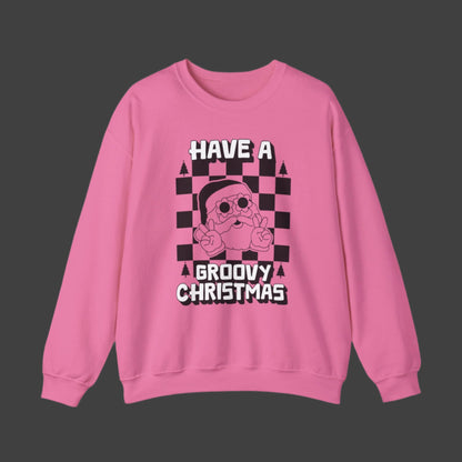 Image: retro Santa christmas sweatshirt available in pink and bright green. The text reads Have a groovy Christmas, with a black checkerboard background, and a vintage Santa wearing daisy sunglasses and giving the peace sign. The perfect gift for those who love a funky vintage aesthetic, by jaecrece