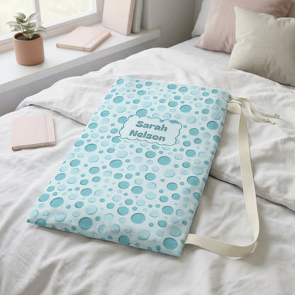 Aqua bubble print drawstring laundry bag styled in a bright laundry room, showcasing its tall rectangular shape, colorful design, and cream fabric drawstrings. Designed for carrying clothing and keeping dirty laundry separate, this dirty clothes sack is suitable for kids, tweens, and teens at home, summer camp, or on overnight trips.