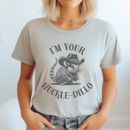 Image: A unisex T-shirt featuring a humorous dark grey illustration of an armadillo dressed as a sheriff, complete with a cowboy hat and jacket. The hat has a small Texas emblem on the brim, adding a fun southern touch. This unique design is perfect for animal lovers, western fashion fans, and anyone who appreciates quirky Texas-themed apparel. A great gift for country style enthusiasts or armadillo fans looking for a lighthearted and stylish shirt, by jaecrece.