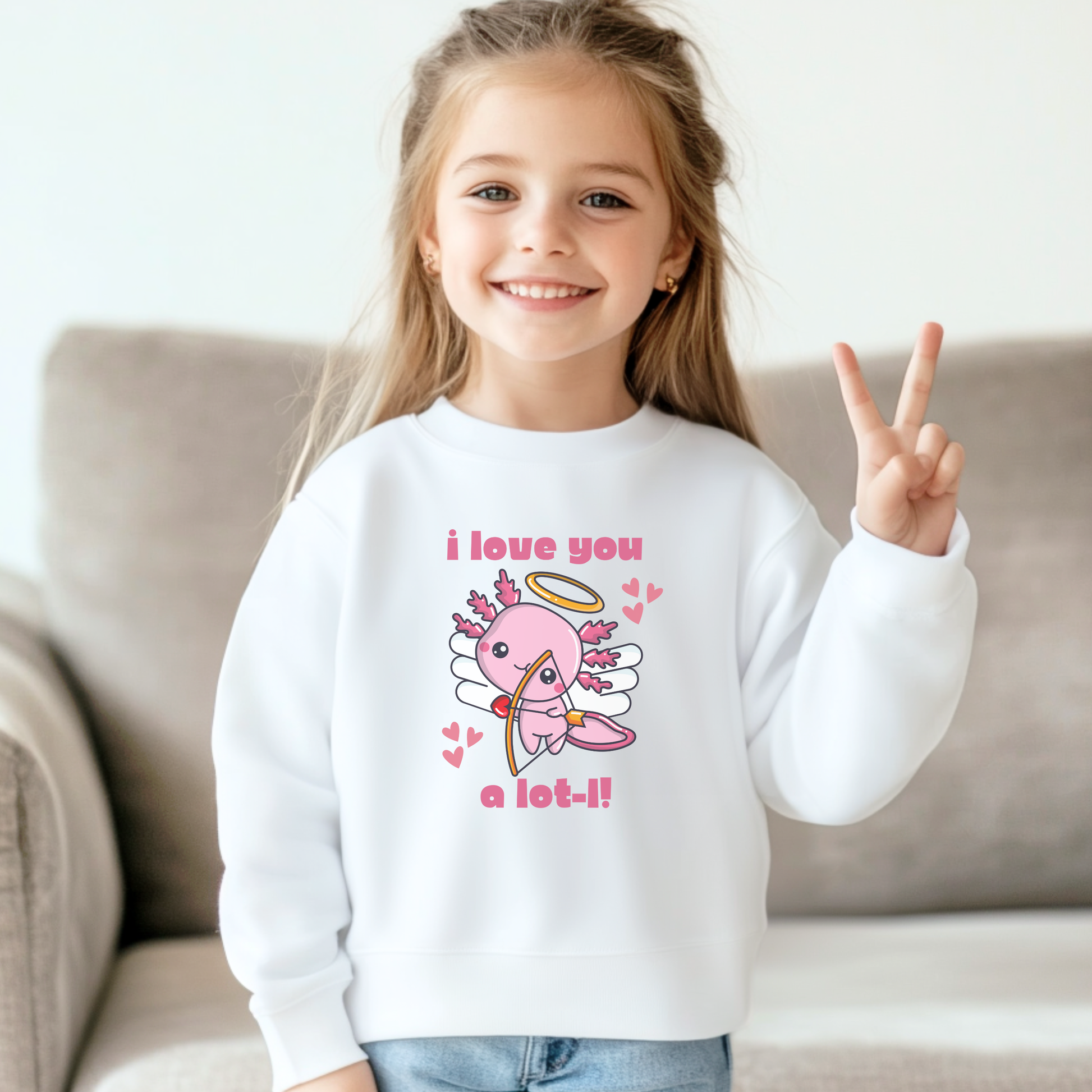 A young girl wearing a white youth Valentine sweatshirt featuring a colorful axolotl cupid graphic with wings, halo, and playful heart details alongside the phrase I love you a lot l. The light fabric color makes the Valentine design stand out while offering a cozy crewneck fit. Ideal for school Valentine parties, festive outfits, and family matching looks.