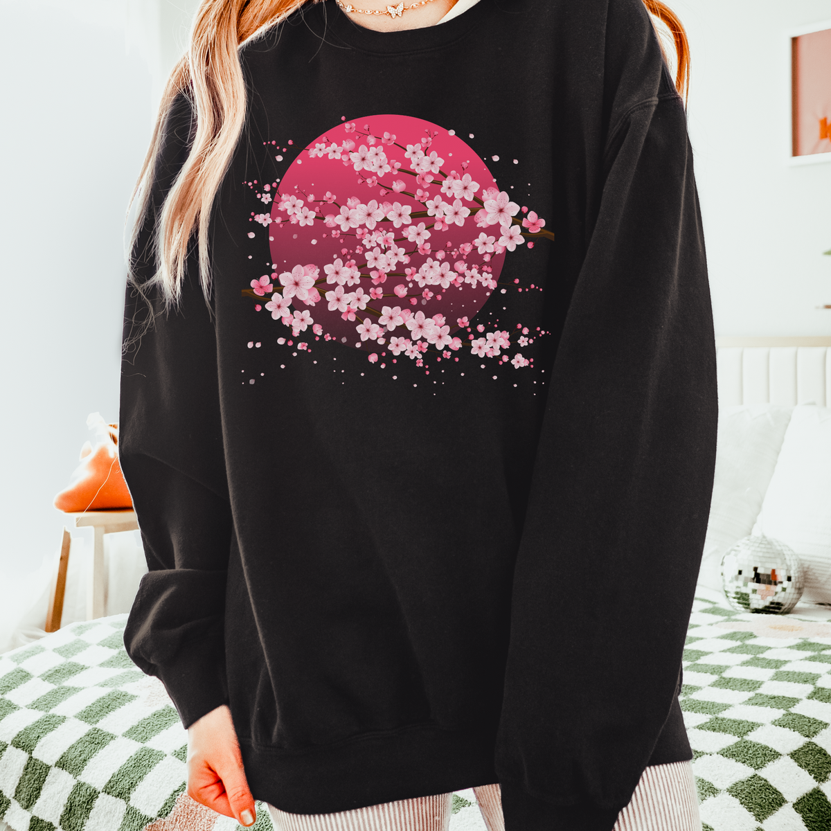 Black Comfort Colors sweatshirt with a soft pink moon surrounded by delicate cherry blossom branches and sakura flowers, creating a striking contrast between the dark neutral sweatshirt and feminine floral artwork. This relaxed women’s pullover blends cozy casual style with romantic Japanese inspired details and is easy to pair with jeans, leggings, boots, or layered fall outfits.