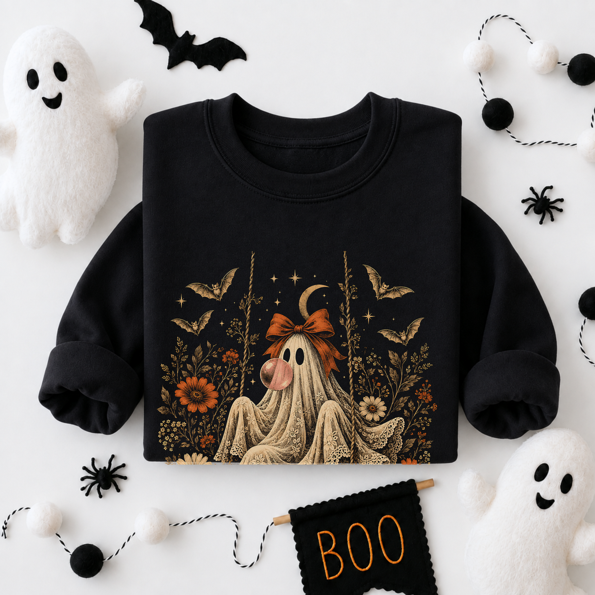 Black girls Halloween sweatshirt shown in a flatlay featuring a vintage inspired ghost blowing a bubble with bubble gum. The detailed artwork includes orange flowers, botanical foliage, bats, stars, lace and a bow, creating a whimsical vintage Halloween design for spooky season outfits.