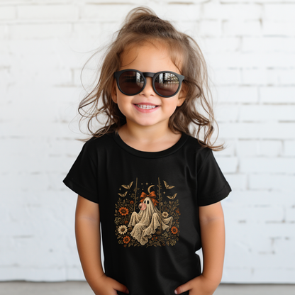 Toddler girl wearing a black Halloween T shirt with a whimsical ghost blowing bubble gum, surrounded by orange flowers, botanical foliage, bats, stars, lace and a bow. A vintage inspired spooky season shirt for toddlers, perfect for fall activities, Halloween celebrations and everyday wear.


