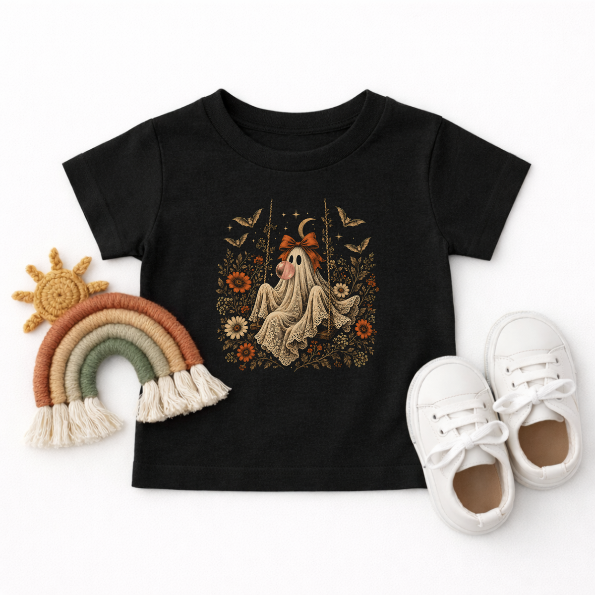 Black toddler Halloween T shirt shown in a flatlay featuring a vintage inspired ghost blowing a bubble with bubble gum. The detailed graphic includes orange flowers, botanical foliage, bats, stars, lace and a bow, creating a cute spooky season shirt for toddlers and little ones who love Halloween.