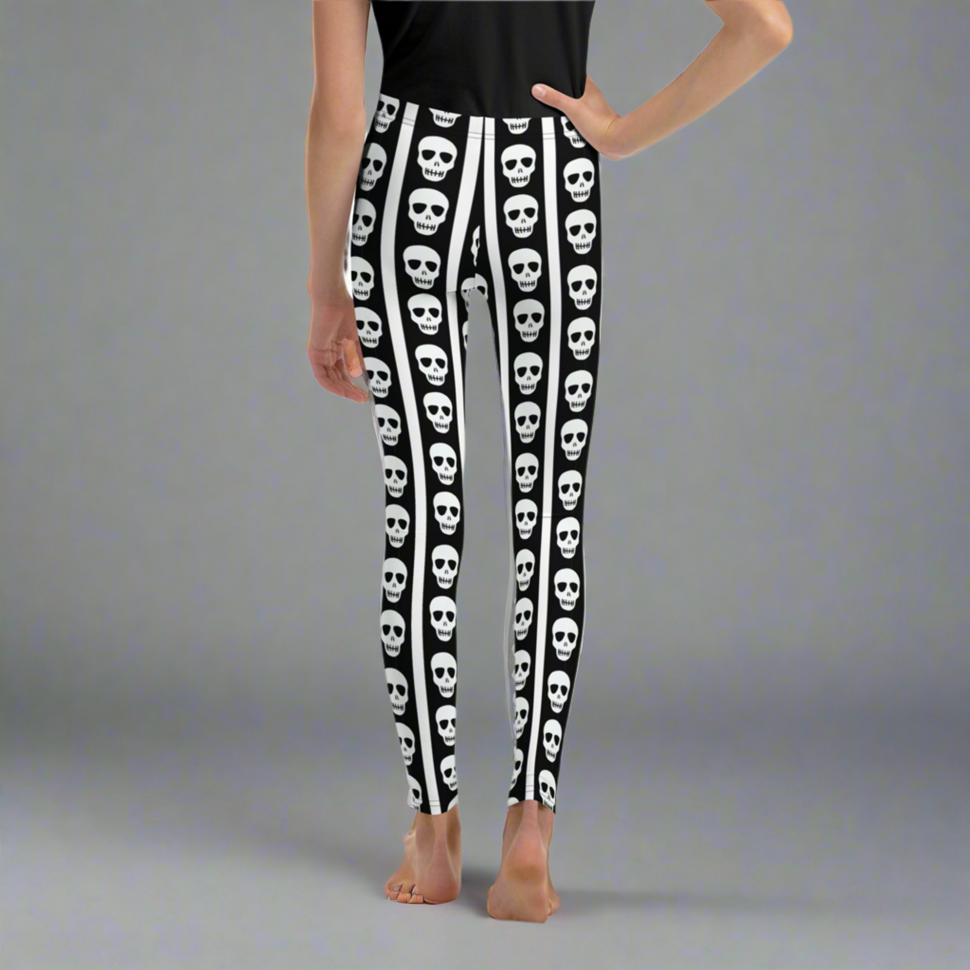 Black and white skull youth leggings featuring repeating skull pattern between vertical stripes. Trendy leggings for girls and tweens sizes 8 to 20 designed for comfort and all day wear. Perfect Halloween outfit for tweens, school fall fashion, or casual spooky aesthetic style. Soft stretchy fabric ideal for active kids who love gothic inspired clothing and fun seasonal statement outfits.