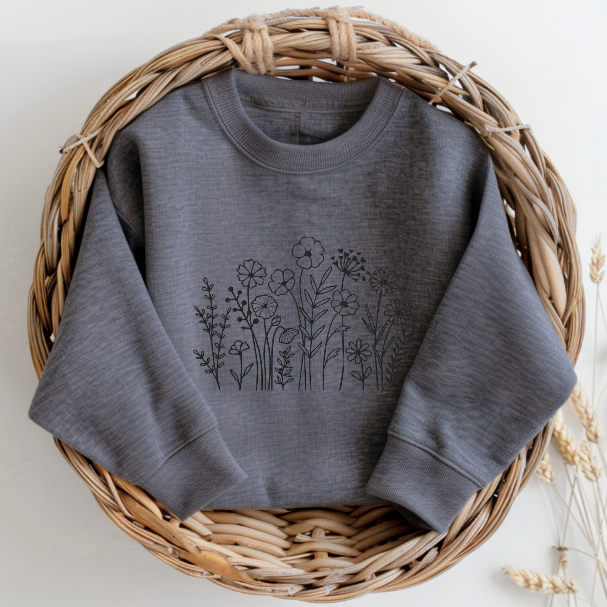 Image: A cozy dark grey sweatshirt with delicate black wildflower embroidery across the chest, showcasing a minimalist yet elegant botanical design. The soft fabric drapes effortlessly, offering comfort for everyday wear. This floral nature crewneck is perfect for layering, adding a subtle floral charm to casual outfits. A thoughtful gift for plant lovers or those who appreciate nature-inspired fashion, by jaecrece.
