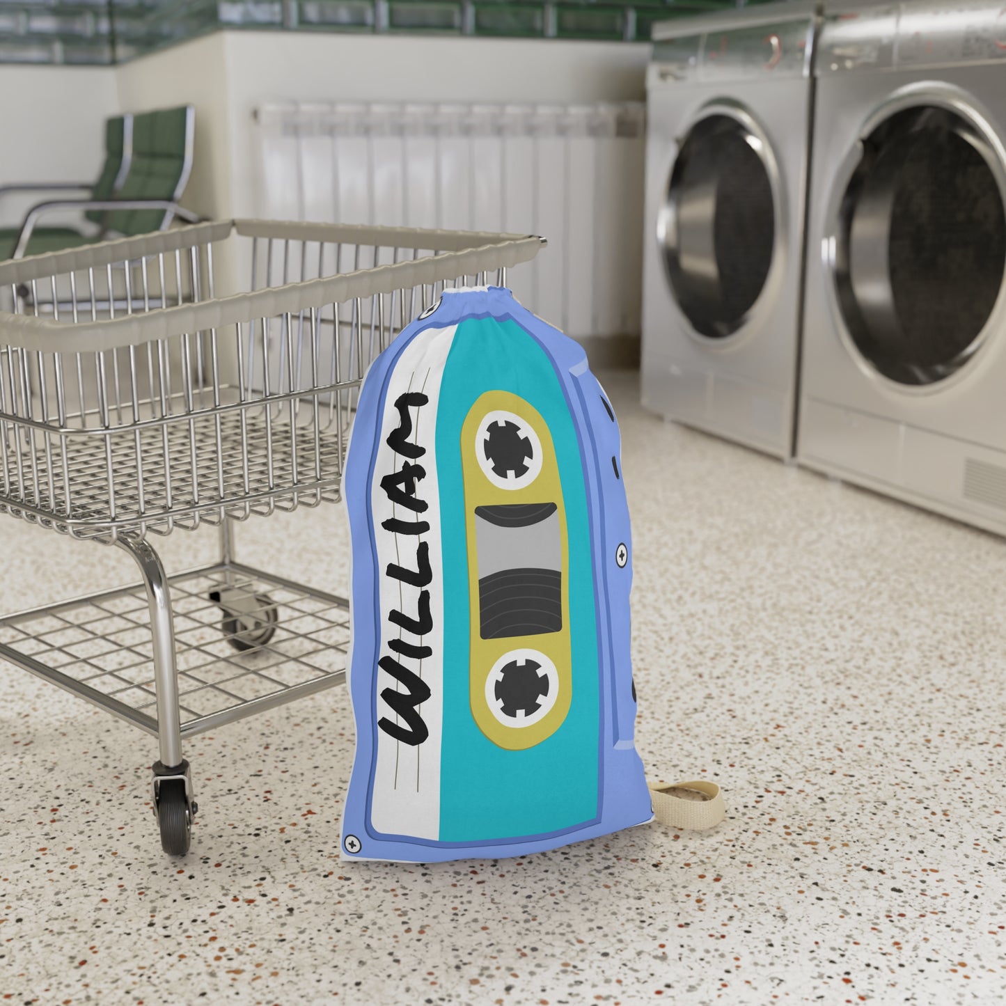 Personalized blue laundry bag featuring colorful cassette tape illustrations and a custom name printed across the fabric. The 18 x 29 inch bag includes a drawstring closure at the top and a woven shoulder strap for convenient carrying. Retro music inspired artwork covers the surface in bright shades of blue, pink, yellow, and teal. Spacious design provides room for clothing, towels, bedding, and camp essentials while adding a playful vintage touch to everyday organization.