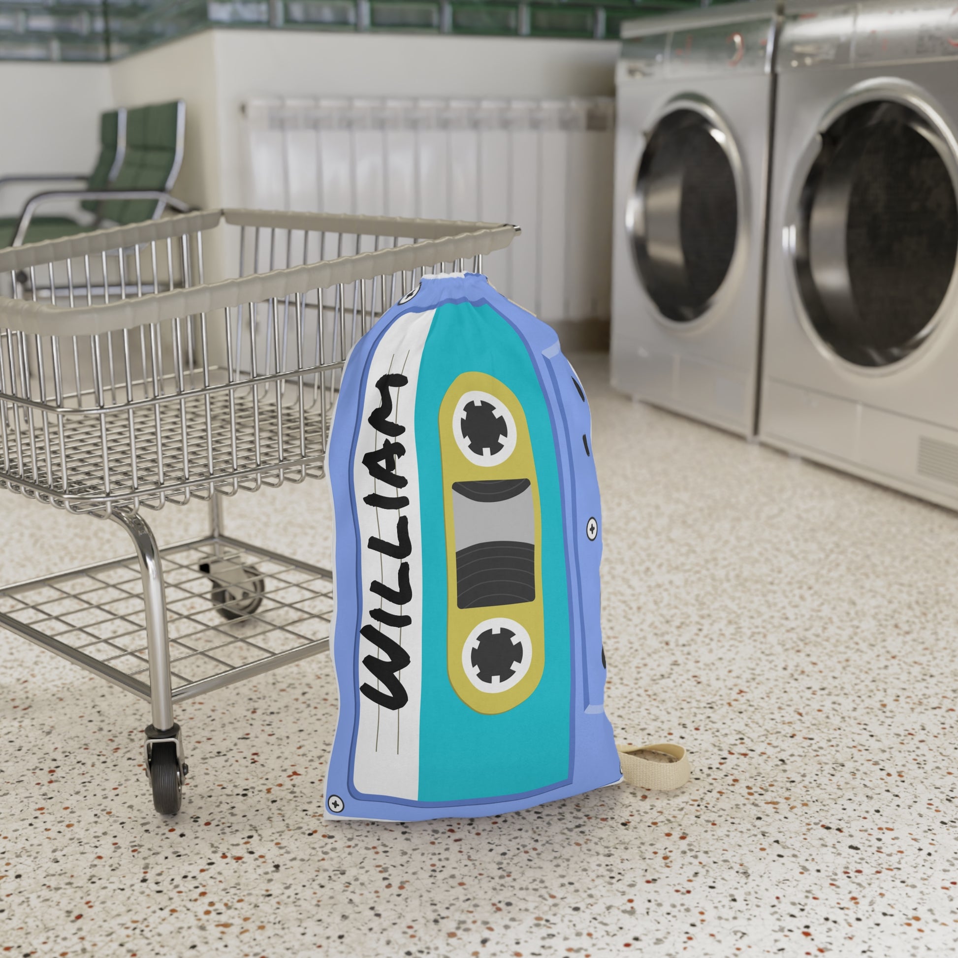 Personalized blue laundry bag featuring colorful cassette tape illustrations and a custom name printed across the fabric. The 18 x 29 inch bag includes a drawstring closure at the top and a woven shoulder strap for convenient carrying. Retro music inspired artwork covers the surface in bright shades of blue, pink, yellow, and teal. Spacious design provides room for clothing, towels, bedding, and camp essentials while adding a playful vintage touch to everyday organization.