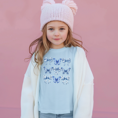 Image: Blue Toile Butterflies and Bows girls T-shirt, made from soft Comfort Colors cotton in shades Chambray, White, True Navy, or Pepper. Sizes XS to XL. Designed with vintage flair and trending soft girl appeal, this shirt features a lovely print ideal for family gatherings or weekend wear. Pair it with denim, skirts, or matching pieces for a full look, by jaecrece.