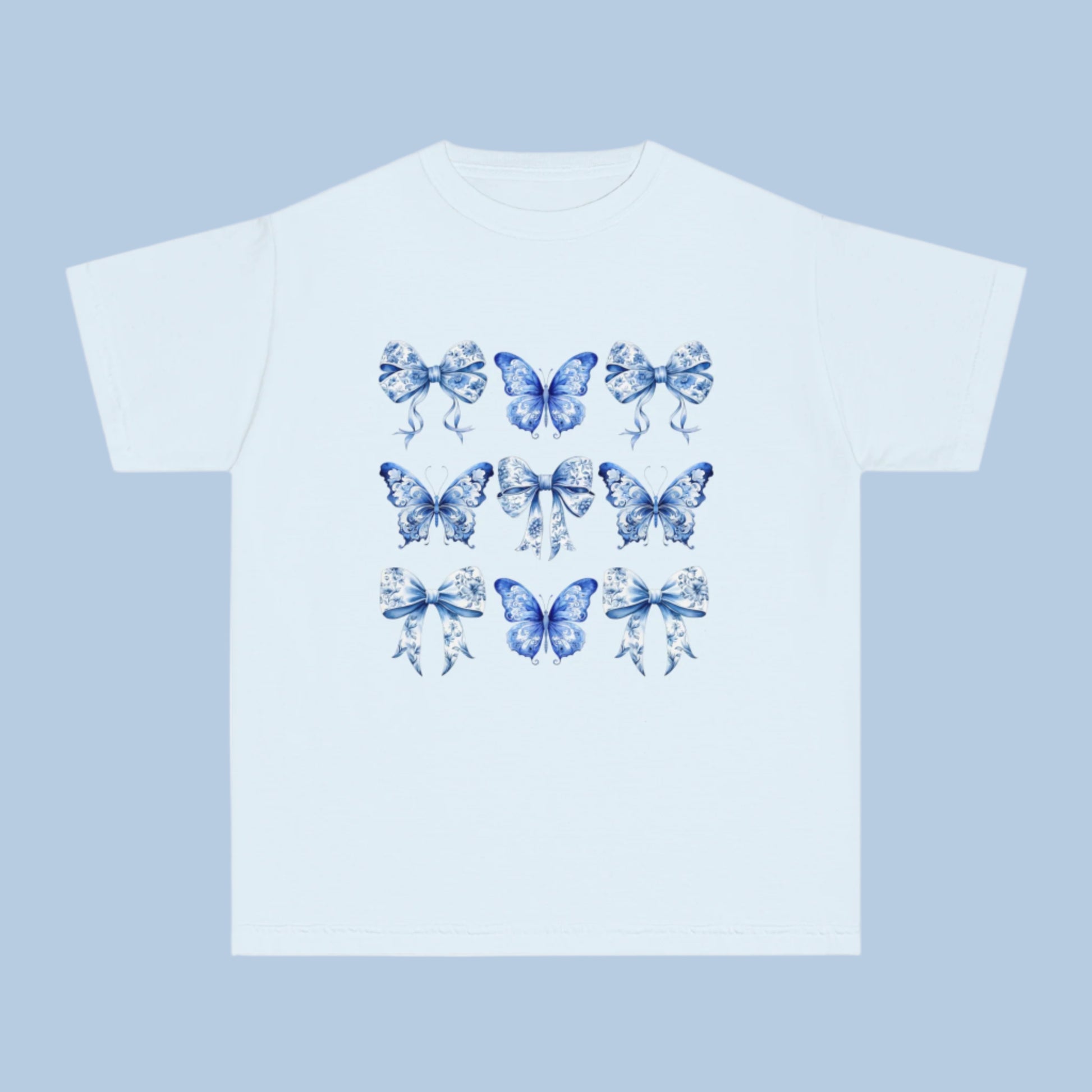 Image: Classic girls’ Comfort Colors T-shirt with a dreamy Blue Toile Butterflies & Bows print, perfect for teens and tweens who love vintage charm, butterfly fashion, or trending coquette aesthetic. Sizes XS–XL available in Chambray, White, True Navy, and Pepper. A soft girl staple and perfect for southern events or casual wear. Coordinates with women’s and toddler leggings or tees for mommy and me outfits, by jaecrece.
