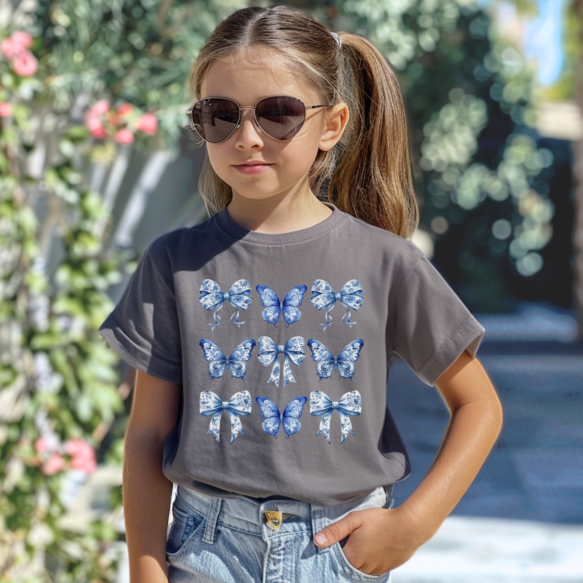 Image: A youth girls’ T-shirt that captures the heart of southern charm and vintage design, this Comfort Colors tee features a toile print of butterflies and bows in soft blue. Sized XS to XL and available in Chambray, White, True Navy, and Pepper, it is a perfect mix of Texas coquette and modern comfort. Match with coordinating family pieces for a full look, by jaecrece.