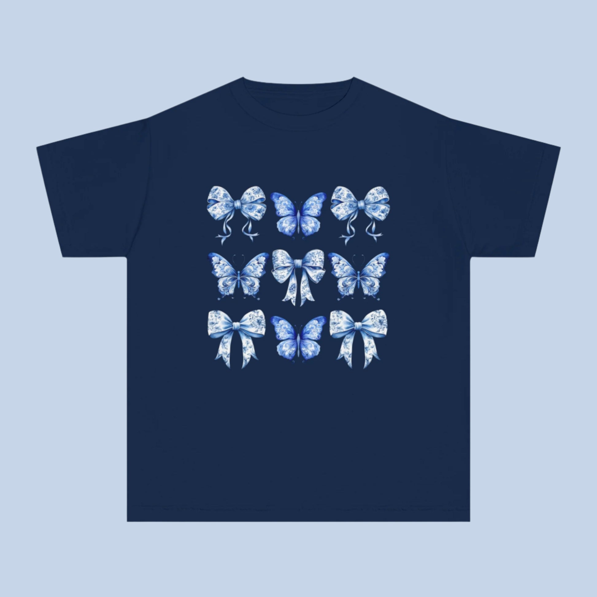 Image: Southern-inspired youth Comfort Colors tee featuring a delicate blue toile of butterflies and bows. Sizes XS–XL available in trendy soft girl shades Chambray, White, True Navy, and Pepper. Great gift idea for birthdays, spring events, or matching family looks. A must-have for Texas girls who love coquette fashion and dreamy countryside style. Soft-washed for comfort and durability, by jaecrece.
