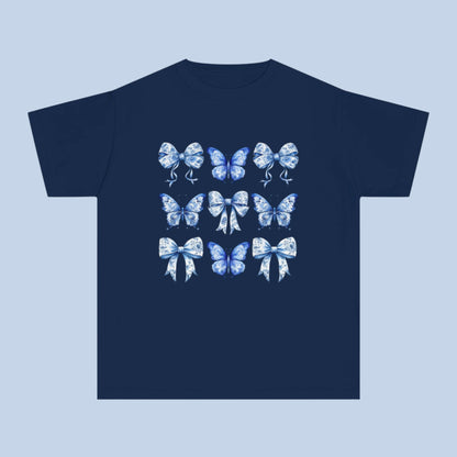Image: Southern-inspired youth Comfort Colors tee featuring a delicate blue toile of butterflies and bows. Sizes XS–XL available in trendy soft girl shades Chambray, White, True Navy, and Pepper. Great gift idea for birthdays, spring events, or matching family looks. A must-have for Texas girls who love coquette fashion and dreamy countryside style. Soft-washed for comfort and durability, by jaecrece.