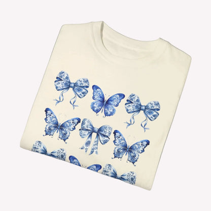 Image: This women’s tee showcases a romantic blue toile pattern filled with fluttering butterflies and dainty bows, tailored for fans of the soft girl and bougie mama aesthetic. Inspired by French toile de jouy and reimagined with a coastal cowgirl twist, it’s a versatile piece made for everyday wear or matching family looks. Coordinates with toddler and youth options for unforgettable photos, by jaecrece.