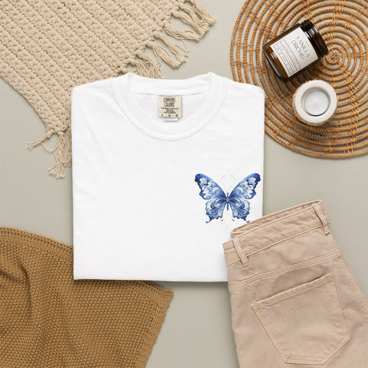 Comfort Colors 1717 oversized tee for women featuring a delicate blue toile butterfly on the left chest pocket area. Soft garment dyed shirt available in five colors and sizes S through 4XL. This chinoiserie inspired butterfly design blends French country charm with quiet luxury style. Perfect for casual outfits, coastal grandmother looks, cottagecore fashion, clean girl basics, summer travel wardrobes, boutique gifts, and everyday relaxed comfort with vintage elegance.