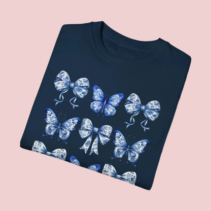 Image: With its dreamy butterfly and bow motif set against a vintage-inspired blue toile background, this women’s shirt blends soft girl style with French country elegance. A staple for bougie mamas and fans of the chinoiserie trend, it’s the perfect tee for family gatherings or spring strolls. Match it with girls’ and toddler sizes for an Instagram ready mother daughter look, by jaecrece.