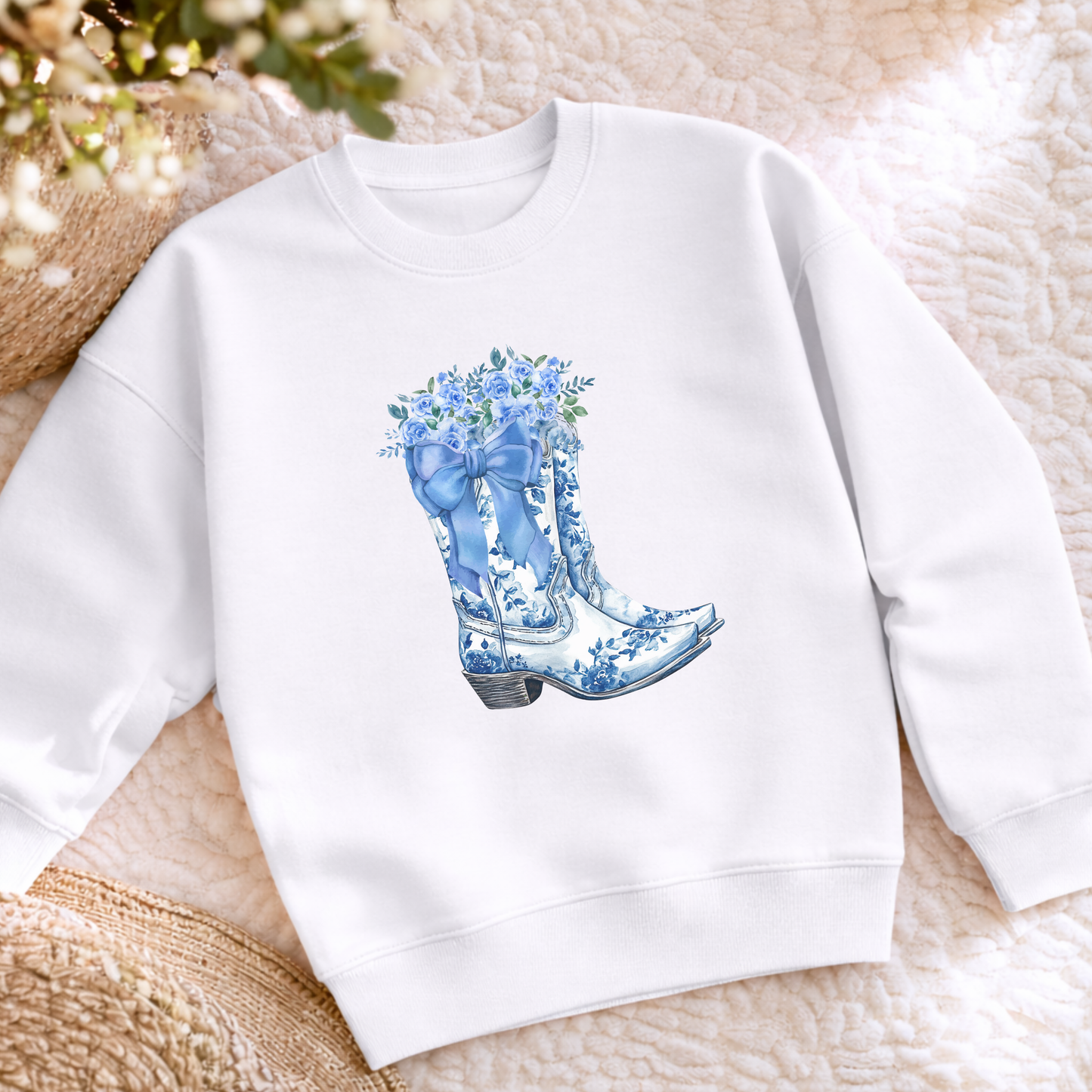 Flatlay showing a blue toile boots sweatshirt featuring a detailed floral cowboy boot graphic inspired by traditional toile patterns. This cozy girls crewneck is a cute choice for school outfits, casual weekends, family activities and anyone who loves feminine Western and country style.