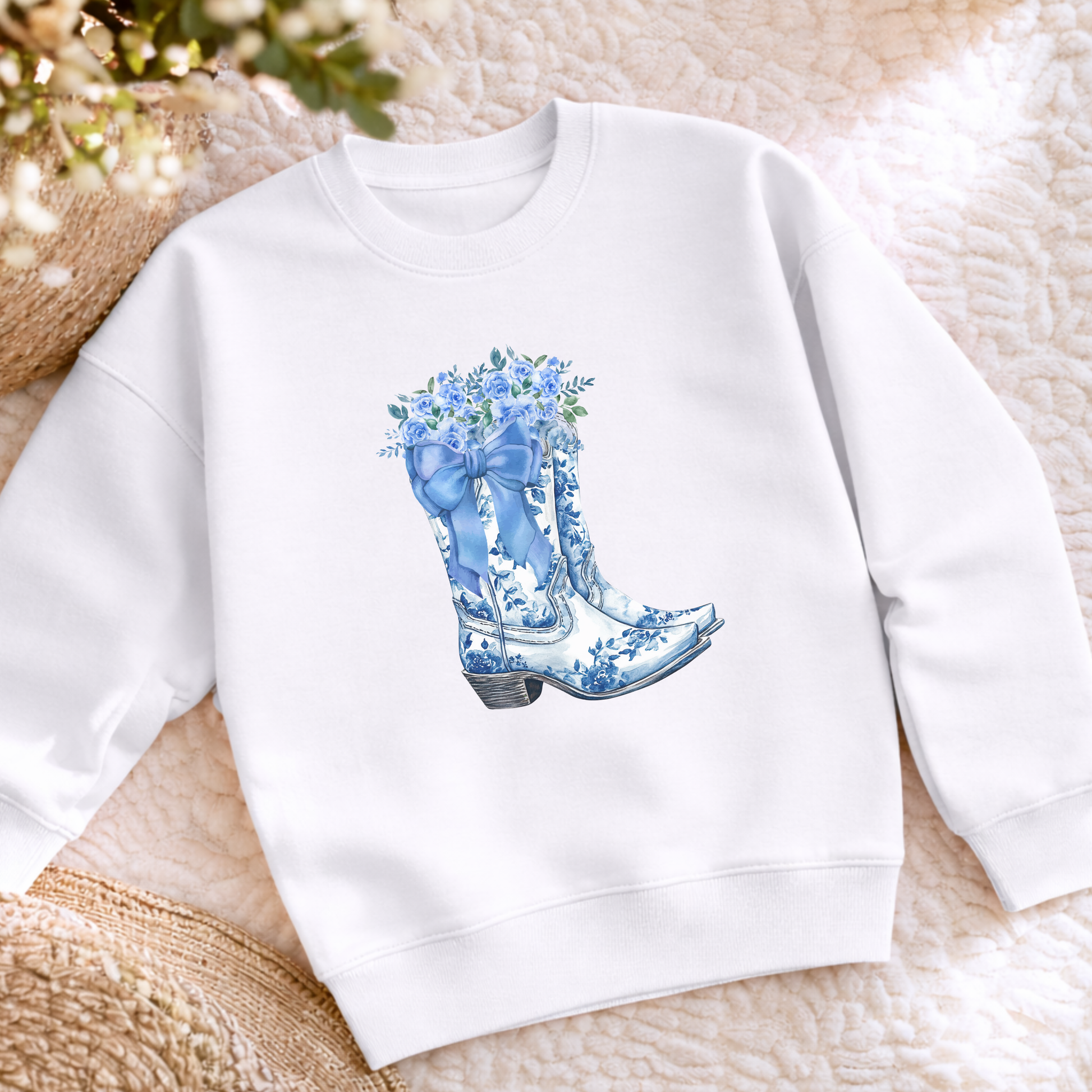 Flatlay showing a blue toile boots sweatshirt featuring a detailed floral cowboy boot graphic inspired by traditional toile patterns. This cozy girls crewneck is a cute choice for school outfits, casual weekends, family activities and anyone who loves feminine Western and country style.