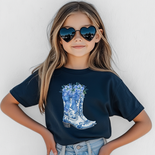 Image: This girls’ blue toile shirt in youth sizes S through XL features western inspired boots with a pretty blue bow and soft wildflowers. With a sweet country flair and coastal cowgirl style, this pullover is perfect for fashion loving girls. Whether heading to school, a rodeo themed birthday, or lounging at home, it adds charm to every outfit and makes a great gift, by jaecrece.
