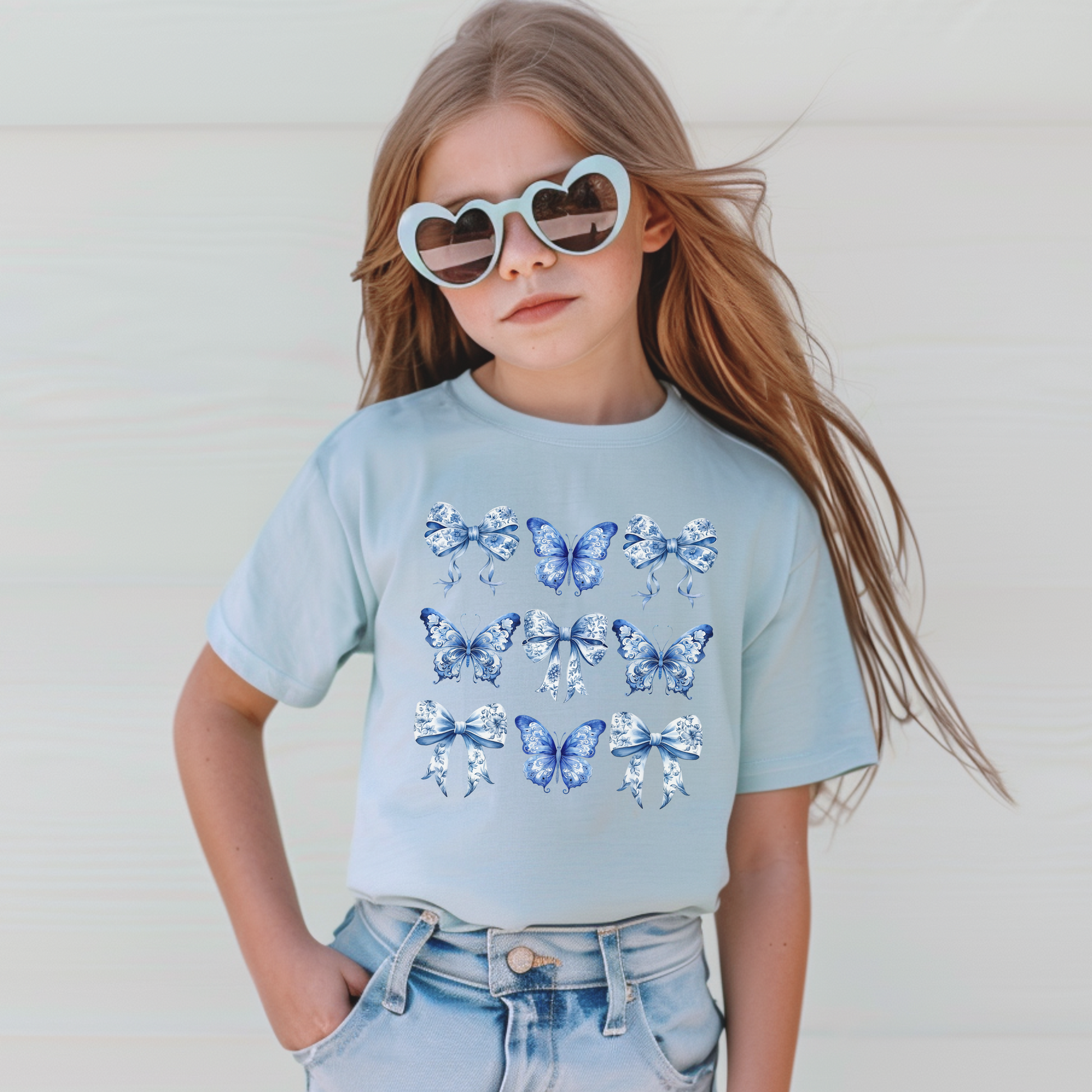Image: Vintage aesthetic girls T-shirt with southern charm and trending coquette vibes. This Comfort Colors tee features blue toile with butterflies and bows in a range of hues including Chambray and True Navy. Available in youth sizes XS to XL. Designed for girls who love timeless prints, spring fashion, or dressing like mom. A cozy, classic piece to wear year-round, by jaecrece.