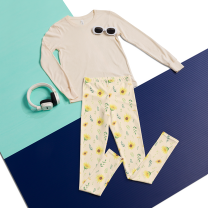 Girls yoga pants featuring a botanical wildflower print with yellow sunflowers, green foliage and smaller flowers scattered across a creamy background. The soft stretchy fabric allows comfortable movement during yoga, stretching, play and everyday activities. The high rise waistband and full length design make them easy to wear with casual tops and sneakers. The cottagecore floral pattern adds a cheerful nature inspired touch to an everyday girls wardrobe.