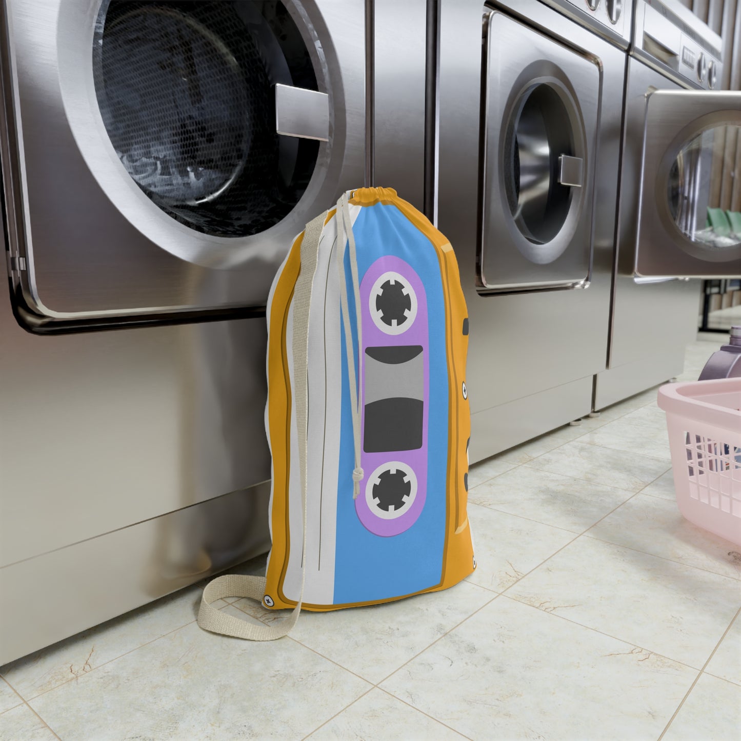 Orange personalized laundry bag covered in colorful cassette tape illustrations with a custom name displayed on the front. The spacious 18 x 29 inch bag features a gathered drawstring closure and woven carrying strap. Retro inspired artwork gives the design a playful music themed appearance. Large capacity makes it useful for clothing, linens, towels, sleepaway camp packing, college dorm storage, or family travel organization.