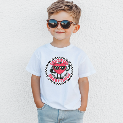 White youth Valentine's Day T shirt shown on a child, featuring a cheerful cartoon heart wearing sunglasses in the center of a black and white checkerboard circle. Certified Heartthrob text surrounds the graphic. The playful design is a fun choice for school celebrations, Valentine's parties, family photos, or everyday wear.