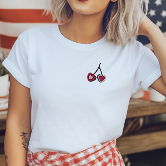 Woman wearing white embroidered cherry hearts t shirt featuring delicate red cherry heart embroidery on the front. Styled in a relaxed fit Gildan S5000 tee, this casual women’s top offers a soft breathable feel and everyday comfort. Perfect for errands, weekend outings, and travel. A matching girls shirt is available separately for mommy and me outfits, creating coordinated family fashion with a sweet minimal aesthetic.