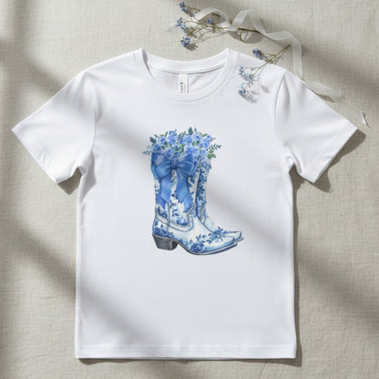 Image: This girls’ shirt brings together western boots, soft florals, and a big blue bow in a toile-inspired design. Sized for kids S through XL, it’s a great choice for young fashionistas who love a mix of country charm and feminine detail. The soft cotton blend offers all-day comfort, making it perfect for school, weekend events, or cozy moments at home, by jaecrece.
