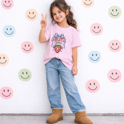 Comfort Colors girls patriotic strawberry t shirt in blossom pink featuring hand drawn strawberry artwork with gingham bow stars and heart accents inspired by America 250 and the 250th anniversary of the United States. Soft relaxed fit youth cotton tee ideal for 4th of July celebrations mommy and me matching outfits summer vacations patriotic family gatherings and vintage Americana kids fashion