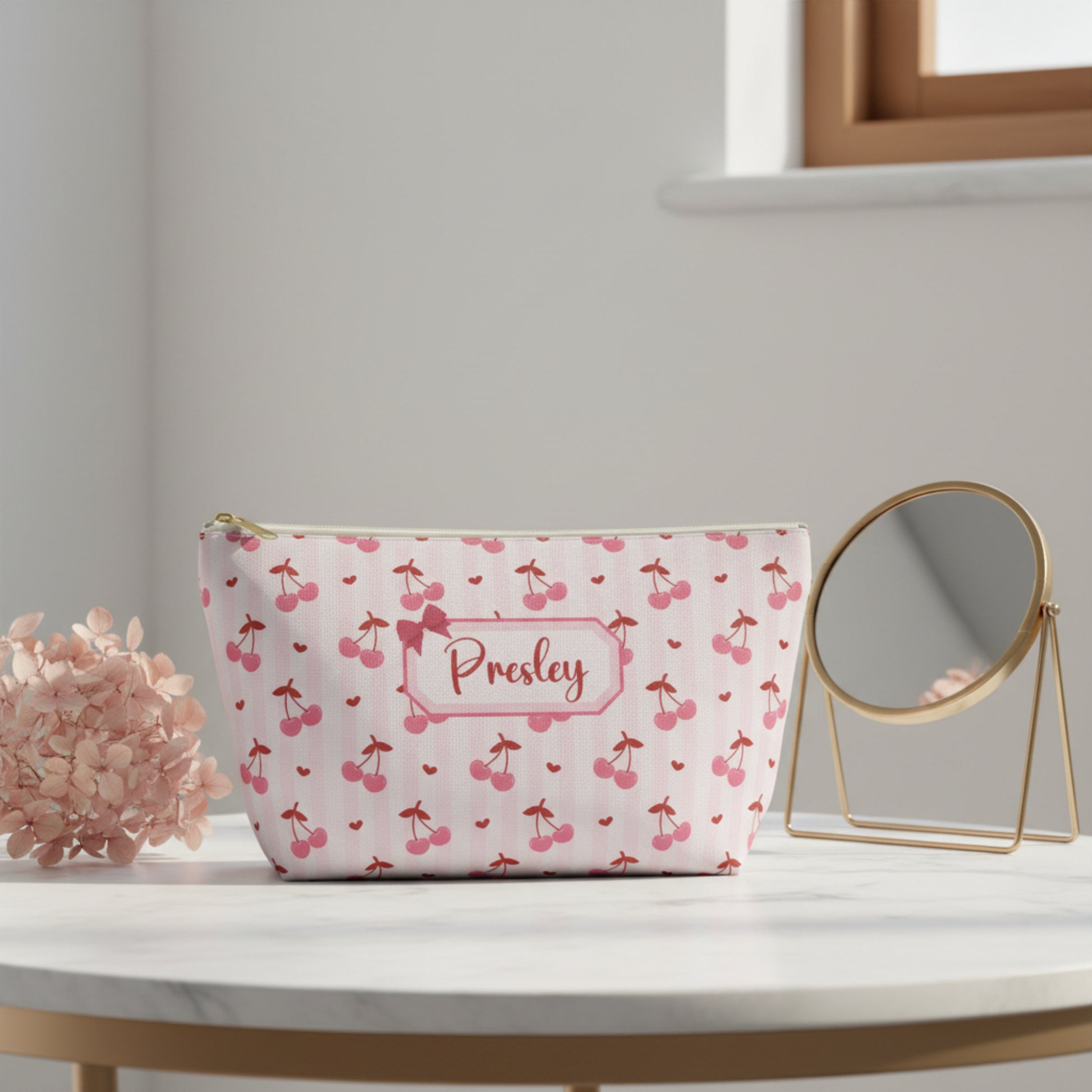 Personalized cherry makeup bag with soft pink background, red cherry pattern, tiny heart details, and custom name label with bow design. Cute coquette cosmetic pouch featuring a white zipper with gold pull and roomy T bottom shape for makeup, skincare, toiletries, lip gloss, chargers, and travel essentials. Feminine soft girl aesthetic accessory bag perfect for teens, tweens, bridesmaids, birthday gifts, stocking stuffers, dance team gifts, and everyday purse organization with Free U.S. Shipping.