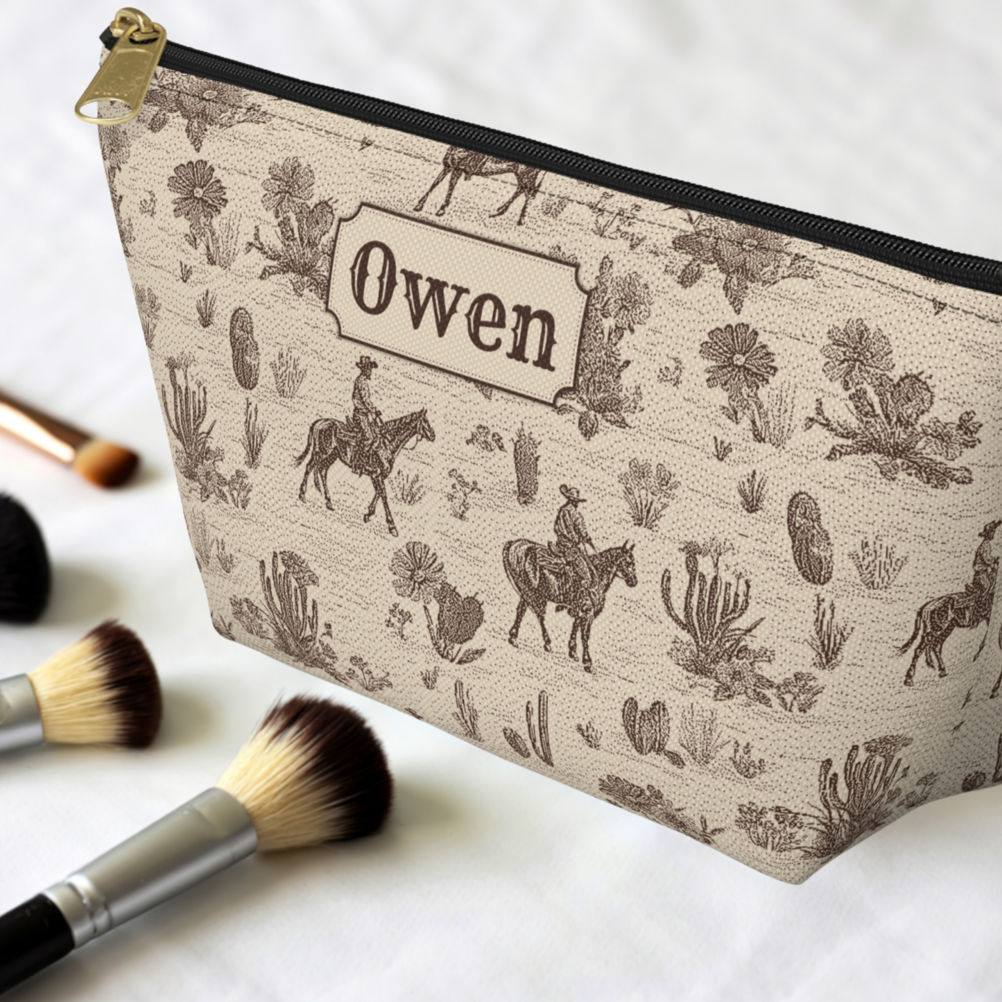 Personalized Western accessory pouch featuring a sepia brown cowboy toile design on a warm cream background. The vintage pattern includes horseback riders, cacti, horses and desert plants. This structured travel pouch works as a Western toiletry bag, grooming organizer, cosmetic bag or everyday accessory case.