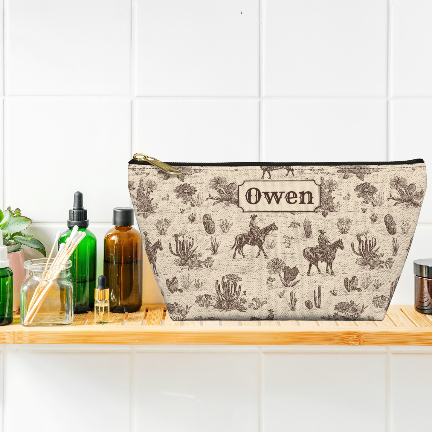 Western toile travel bag personalized with a name and printed in a classic brown and cream color palette. The cowboy inspired toile pattern features ranch riders, horses, cacti and desert plants. The structured T bottom gives this Western accessory pouch extra room for travel toiletries, cosmetics and grooming essentials.