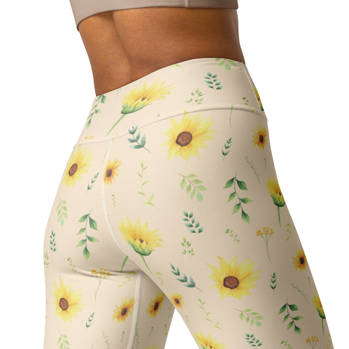 Close view of the sunflower print on women's leggings, showing detailed yellow blooms with warm brown centers surrounded by soft green leaves and delicate botanical sprigs. The cream background keeps the overall design light and feminine while allowing the flowers to stand out. The nature inspired pattern is a lovely choice for anyone who enjoys cottagecore fashion, garden inspired clothing, or botanical prints.