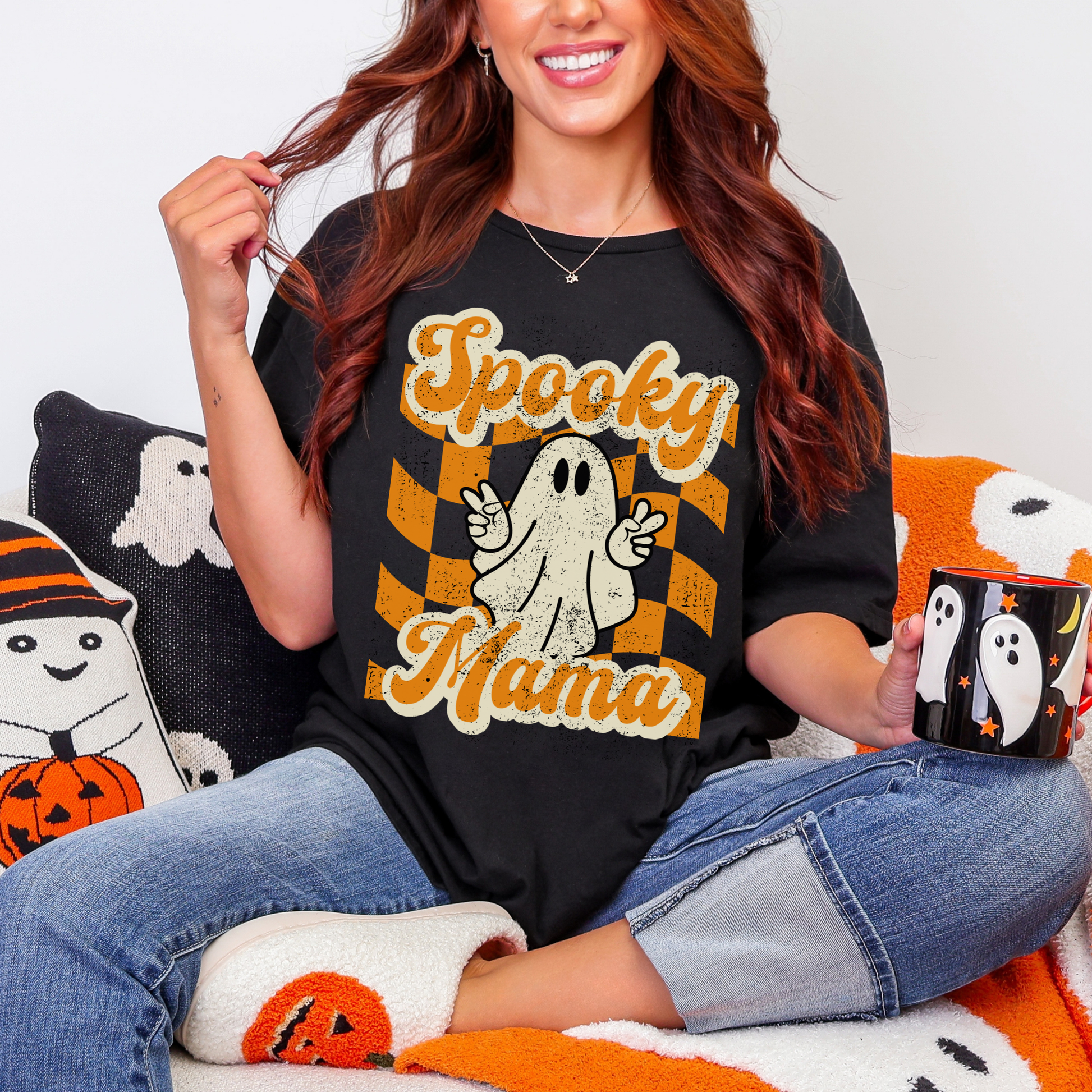 Cute Spooky Mama graphic tee on a black Gildan Softstyle shirt with a smiling ghost flashing peace signs and bold orange checkered design. Trendy Halloween mom shirt made for festive fall outfits, pumpkin patch photos, classroom events, trunk or treat, haunted house trips, and casual everyday wear. Soft breathable fabric with a relaxed fit that styles easily with denim, flannel, joggers, or leggings. Matching mommy and me Spooky Mini shirt available. Free U.S. Shipping.