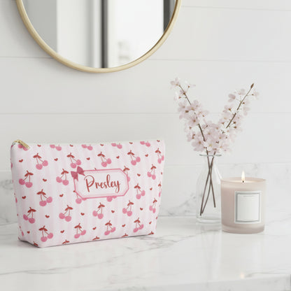 Cute personalized cherry makeup pouch with feminine soft pink and red cherry print designed for coquette, balletcore, and soft girl aesthetics. The structured T bottom cosmetic bag stands upright for easy access to makeup, skincare products, lip balm, hair clips, and travel accessories. Features a smooth white zipper with gold pull and custom name label for a thoughtful personalized touch. Trendy gift idea for teen girls, best friends, bridesmaids, teachers, and pink accessory lovers.