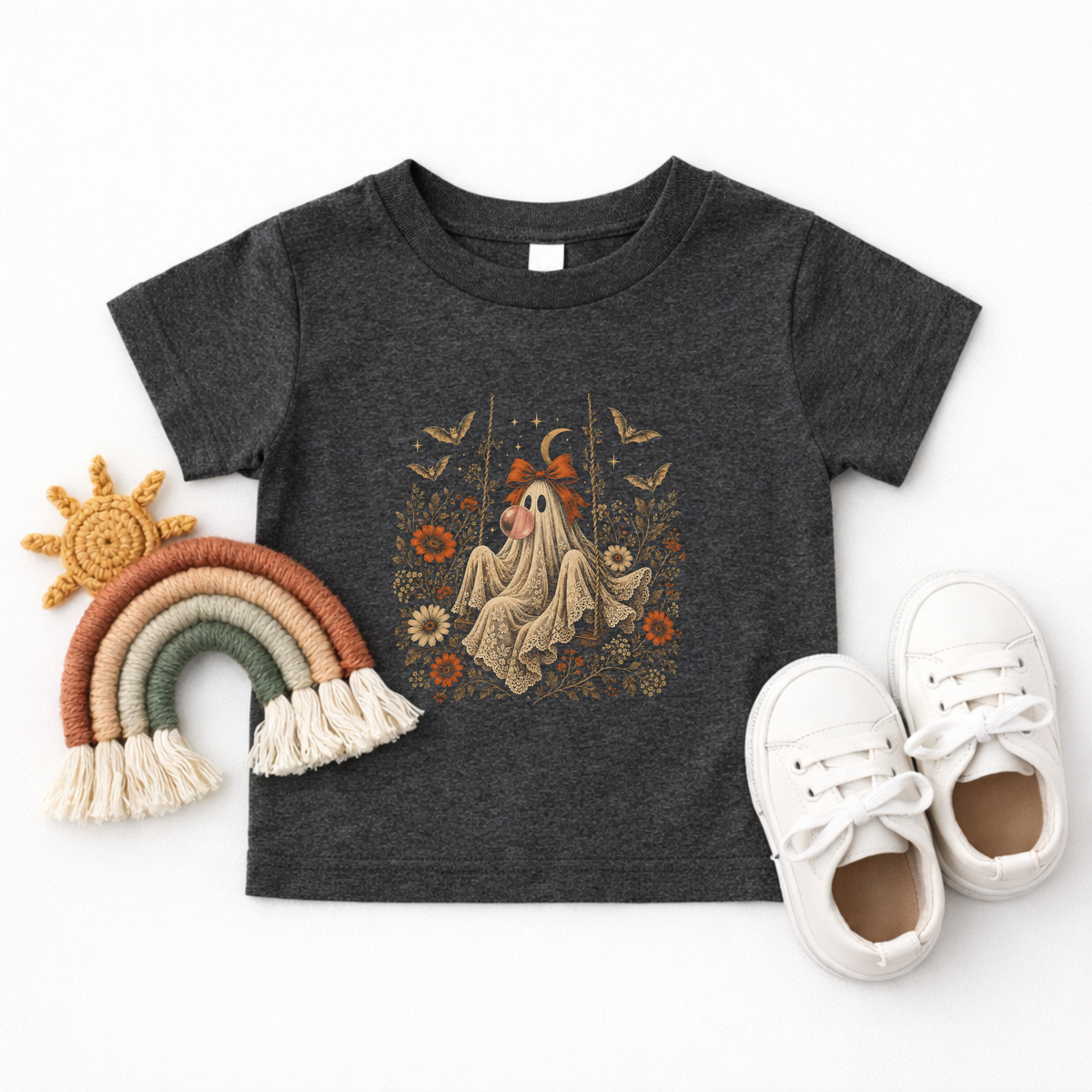 Dark heather grey toddler Halloween T shirt shown in a flatlay featuring a vintage ghost blowing a bubble with bubble gum, surrounded by orange flowers, botanical foliage, bats, stars, lace and a bow. A whimsical spooky season graphic tee for toddlers and little ones who love cute Halloween designs.