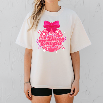 This Comfort Colors Disco Cowgirl shirt for women features a sparkly pink disco ball, bold pink and purple lettering, and a coquette hot pink bow. A fun western-themed t-shirt perfect for bachelorette parties, rodeo season, country concerts, and girls’ trips. The relaxed, vintage fit makes this a festival-ready favorite. Available in black, ivory, white, and pepper, sizes S–4XL.