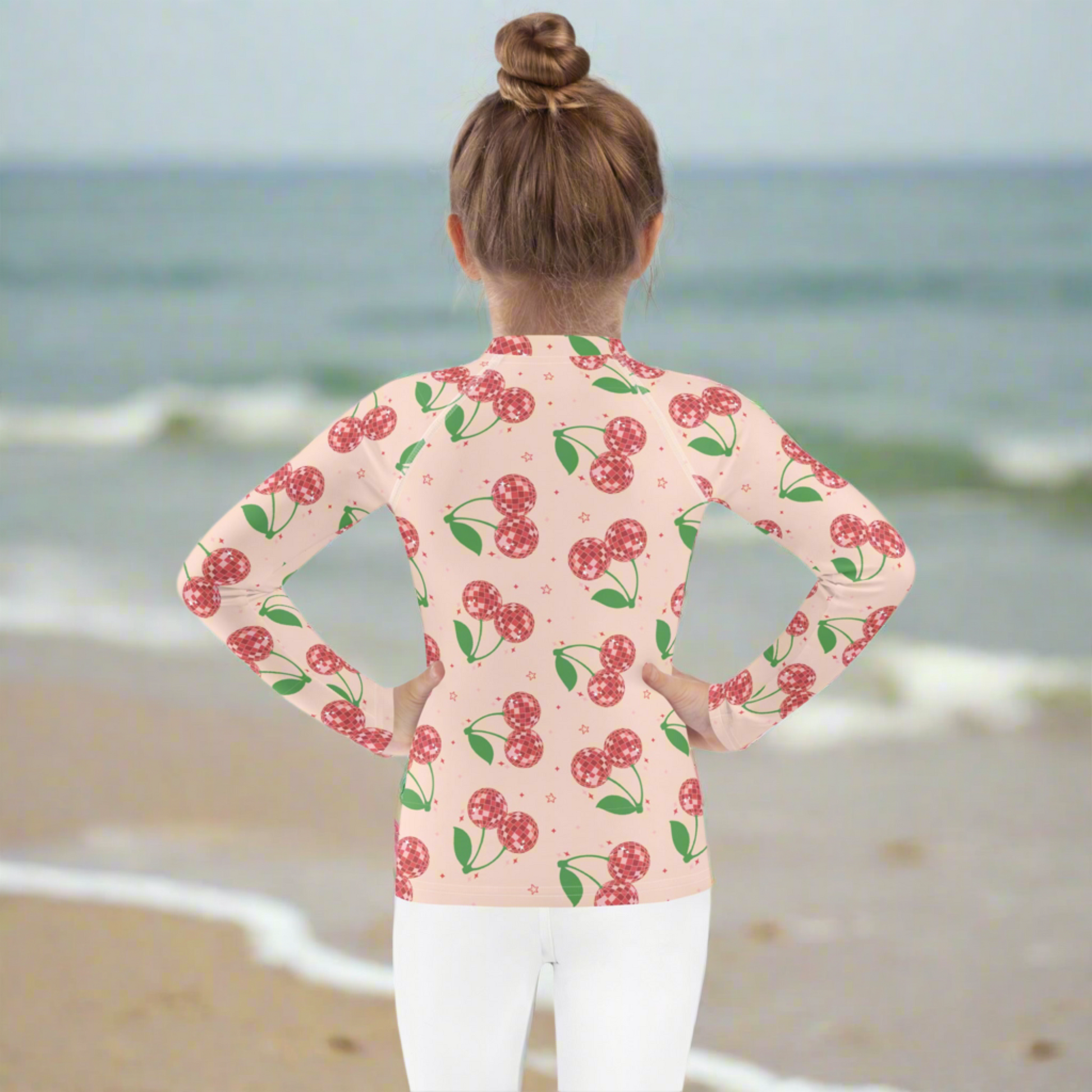 Girls long sleeve swim rash guard in a pink disco cherry print, available in toddler sizes 2T to 7. Designed with a fitted silhouette and UPF 50 protection to keep kids safe in the sun. The soft stretch fabric allows comfortable movement for swimming, beach days, and outdoor play. A playful and trendy kids swimwear option that is also available in matching mommy and me styles for coordinated family outfits.