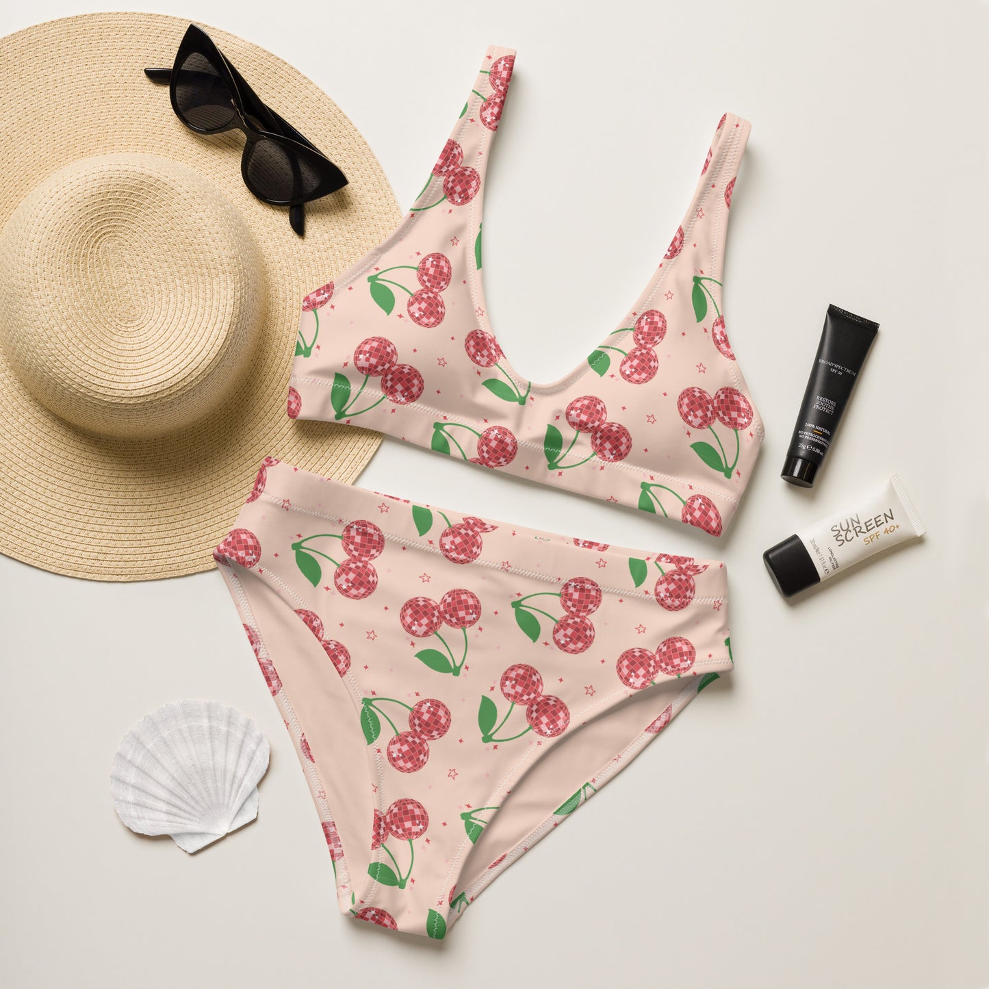 Women's high waisted bikini featuring a playful disco cherry print on a soft blush pink background. The sparkling cherry design combines retro charm with a fun coquette aesthetic, making it perfect for beach vacations and pool days. Made from recycled fabric with a supportive scoop neck top and flattering high rise bottoms, this swimsuit is available in sizes Small through 3XL and coordinates with matching swimwear for the whole family. A thoughtful gift for moms, sisters, daughters, or best friends who lov
