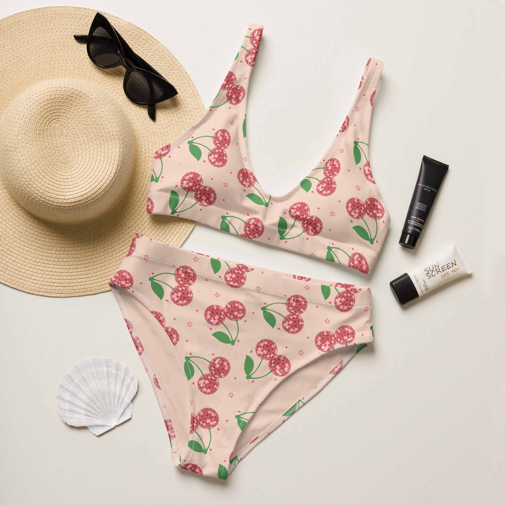 Women's high waisted bikini featuring a playful disco cherry print on a soft blush pink background. The sparkling cherry design combines retro charm with a fun coquette aesthetic, making it perfect for beach vacations and pool days. Made from recycled fabric with a supportive scoop neck top and flattering high rise bottoms, this swimsuit is available in sizes Small through 3XL and coordinates with matching swimwear for the whole family. A thoughtful gift for moms, sisters, daughters, or best friends who lov