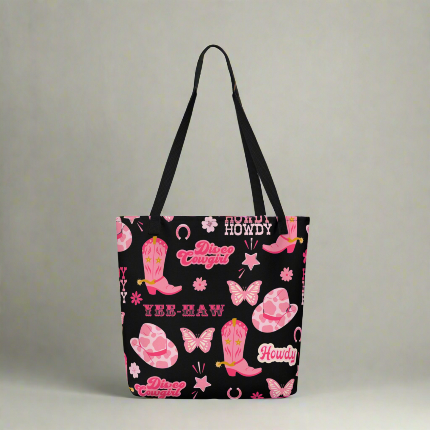 Image: Disco Cowgirl Tote Bag. This western glam canvas shoulder bag has a black background with a pink, white and pink pattern of butterflies, daisies, cowgirl hats and boots. The text on the bag reads Howdy, Yee-Haw and Disco Cowgirl. Great for weekend girls trips or bachelorette parties in Nashville, by jaecrece