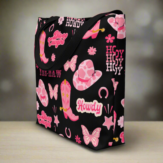 Image: Disco Cowgirl Tote Bag. This western glam canvas shoulder bag has a black background with a pink, white and pink pattern of butterflies, daisies, cowgirl hats and boots. The text on the bag reads Howdy, Yee-Haw and Disco Cowgirl. Great for weekend girls trips or bachelorette parties in Nashville, by jaecrece
