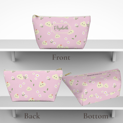 Pastel dumpling makeup bag with a whimsical pattern of smiling dumplings, delicate flowers, and green leaves. A personalized name is printed in elegant Ballerina script using deep sage green lettering that coordinates with the botanical details. This versatile organizer is useful for makeup, skincare, toiletries, hair accessories, chargers, school supplies, and travel essentials.