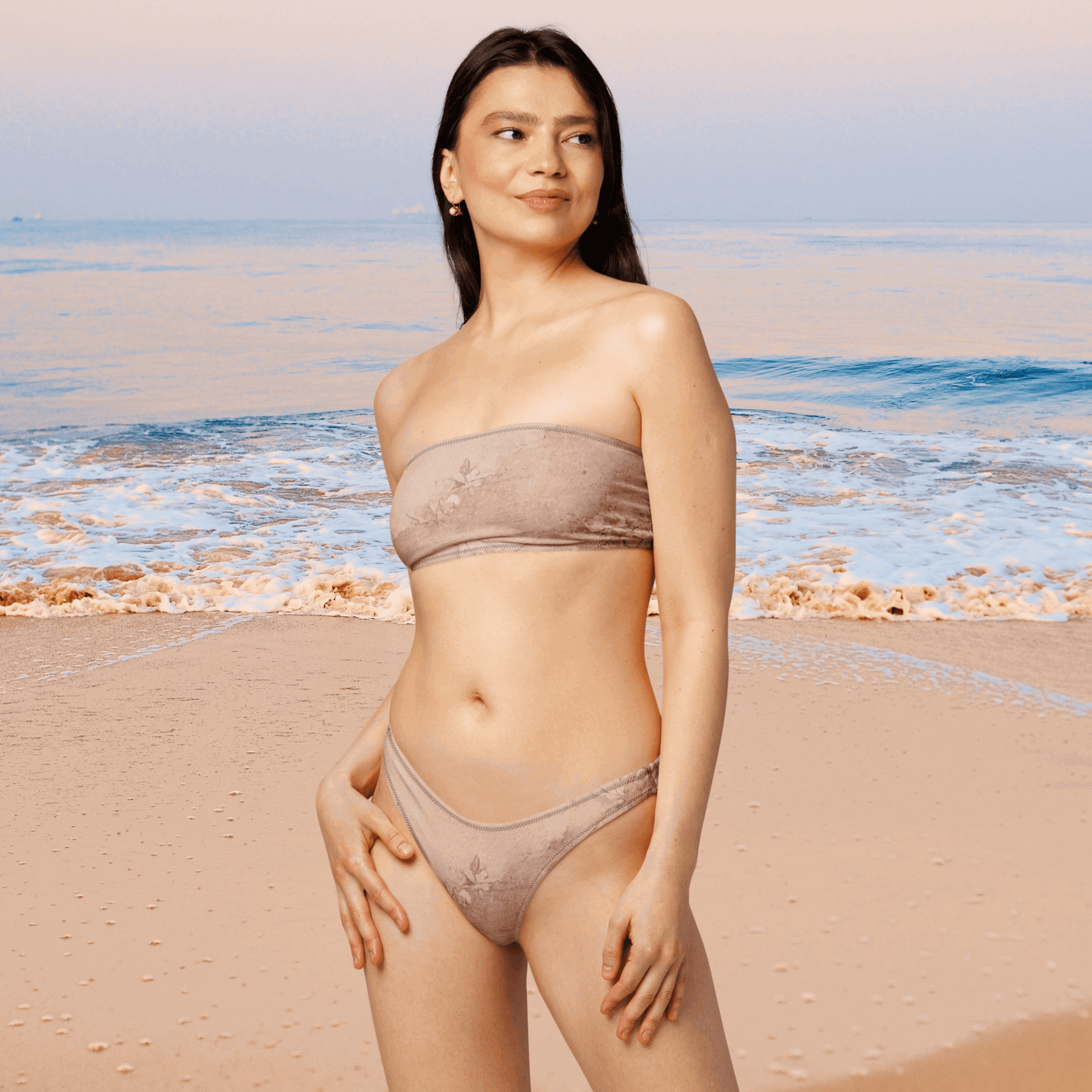Model wears the Dusty Pink Cottagecore Bandeau Bikini at the beach, showing off the flattering V-cut high-leg bottoms and strapless bandeau top. The soft, muted pink hue and recycled fabric make this set perfect for sustainable fashion lovers. This feminine two-piece swimsuit blends modern fit with vintage charm and is available in inclusive sizes 2XS–6XL.