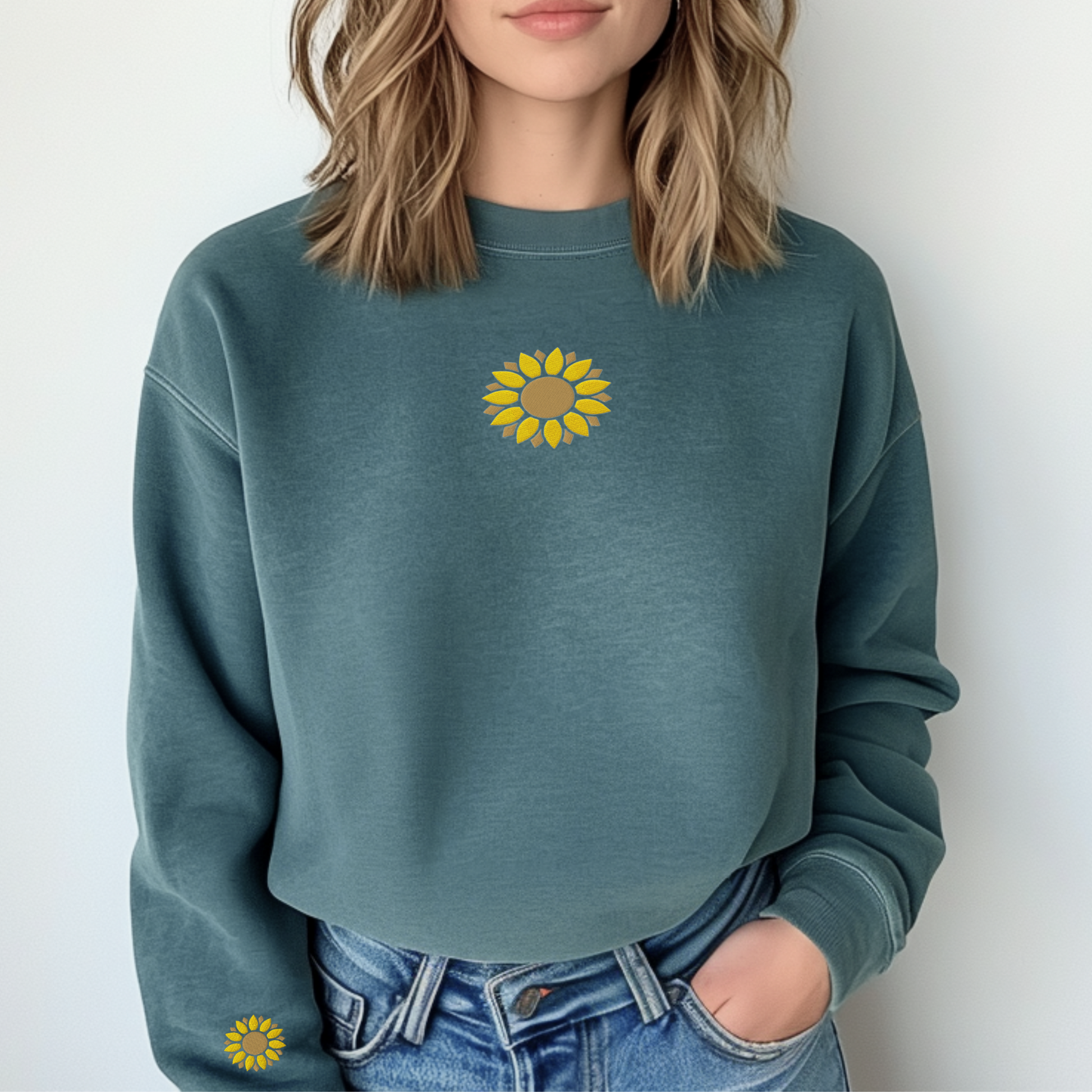 A woman wearing a green sweatshirt with embroidered sunflower motifs on the chest and wrist area, paired with blue jeans.